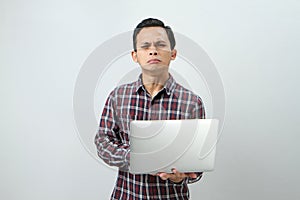 sad expression of asian indonesian man holding laptop computer on  background