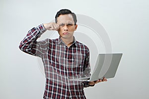 sad expression of asian indonesian man holding laptop computer on  background