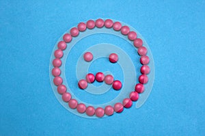 Sad face laid out of pink pills on blue background