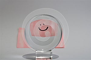 Sad face on a pink post it note looking through a glass ball