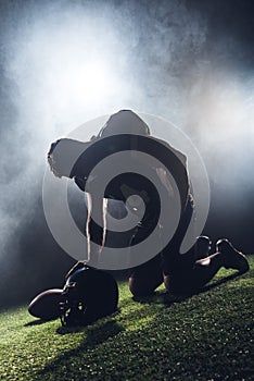 sad failed american football player standing on knees on green grass and looking down against