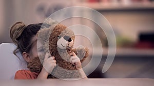 Sad female kid covering face by teddy bear toy, family problem, loneliness abuse