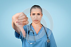 Sad female nurse with thumbs down on blue background