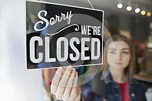 Sad Female Owner Of Small Business Turning Round Closed Sign In Shop Window