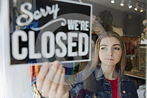 Sad Female Owner Of Small Business Turning Round Closed Sign In Shop Window