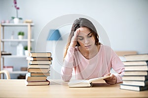 Sad female student reading a book for the exam or doing homework