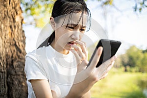 Sad female student victim of cyber bullying online sitting alone outdoor at school,child girl receiving text message at mobile