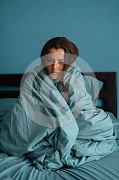 Sad female, worried, suffers from insomnia and headache. Girl sits on bed in bedroom. Migraines, health and mental