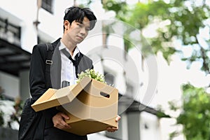 Sad fired businessman holding cardboard box with belongings walking out of the office building