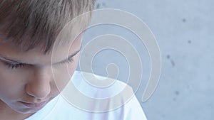 Sad frustraited teenager boy lowered his head standing alone near gray wall and looking to the side. 4k video