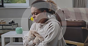 Sad frustrated African American woman sitting at home hugging toy rabbit. Portrait of depressed upset young lonely lady