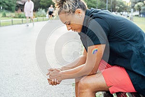 Sad frustrated lesbian woman with LGBTQ rainbow tattoo on her hand sitting on the park bench alone. Concept of