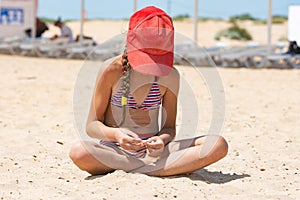 Sad girl on the beach goes to the shells, face covered with a red cap