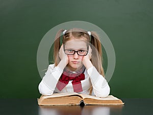 Sad girl with big book near empty green chalkboard