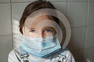 Sad girl with blue eyes in a protective disposable mask stays at home because of the epidemia of Coronavirus Covid-19 in photo