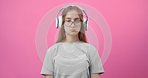 Sad girl in headphones listening music over pink background