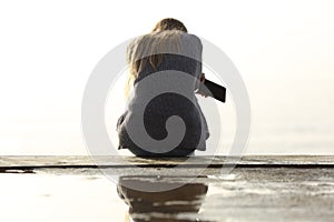 Sad girl holding phone complaining sitting on a ledge