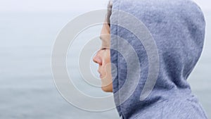 A sad girl in a hoodie walks along the seashore in cloudy weather. Tracking shot