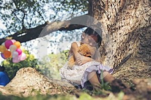 Sad girl hugging teddy bear sadness alone in green garden park. Lonely girl feeling sad unhappy sitting outdoors with best friend