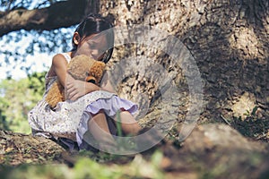 Sad girl hugging teddy bear sitting under tree sadness alone in green park. Lonely girl feeling sad unhappy sit outdoors hug best