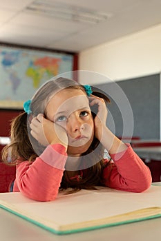 Sad girl leaning on desk in a classroom at school