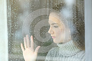 Sad girl looking through a window in a rainy day