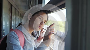 Sad girl looks out the train window. Travel transportation railroad concept. Teen girl misses traveling in a train