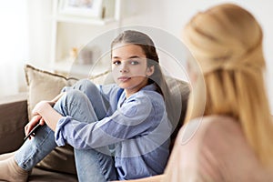 Sad girl with mother sitting on sofa at home