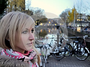 Sad girl in pink jacket near the canal of Amsterdam on blue hour evening among bikes