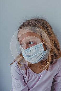 A sad girl in quarantine with a mask looks with blue eyes. the girl wants to go for a walk during the epidemic