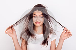 Sad girl showing her damaged hair while standing white background