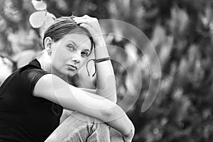 Sad girl sits on a background of foliage and looks sadly into the frame, black and white photography