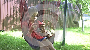 A sad girl sits on a garden swing with a smartphone, vacations, rest, summer cottage.