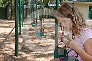 Sad girl sitting alone on a playground swing