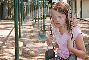 Sad girl sitting alone on a playground swing