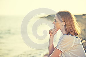 Sad girl sitting on the beach and looks into the distance at se