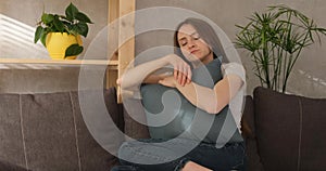 Sad girl is sitting on couch and hugging pillow. Young sorrowful woman feels lonely.