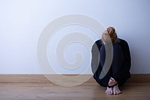 Sad girl sitting curled up on the floor, copy space on empty wall