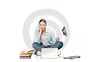 Sad girl sitting on floor with laptop, books and copybooks and holding uk flag