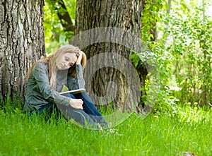 Sad girl sitting on grass and reading a book