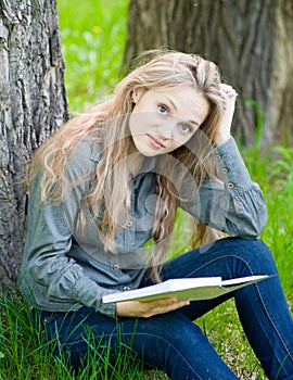 Sad girl sitting on grass and reading a book