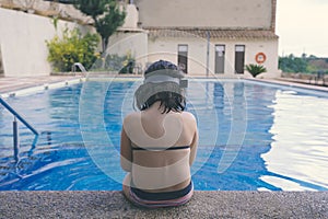 Sad girl sitting lonely at the edge of the pool.