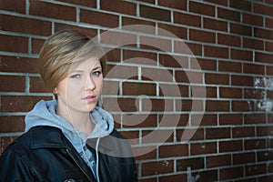 Sad girl sitting outside brick wall in school yar