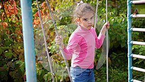 Sad girl on a swing. Young beautiful girl is having fun on a swing. Thoughtful child swinging on a rope swing. 4k, 60fps