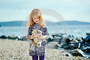 Sad girl with a toy is on the beach or lake