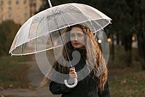 Sad girl with umbrella in autumn park. November seasonal portrait. Young woman with long brown heir under umbrella