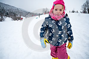 Sad girl wearing pink hat at snowy slope.