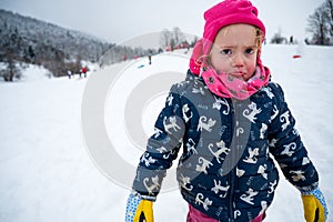 Sad girl wearing pink hat at snowy slope.