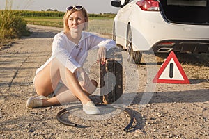 Sad girl whose driver has run out of gasoline in a car on a rural road sits waiting for help with a fuel canister