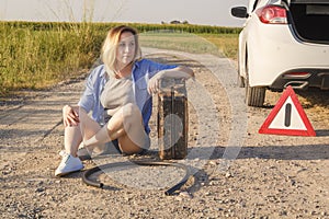 Sad girl whose driver has run out of gasoline in a car on a rural road sits waiting for help with a fuel canister and a hose